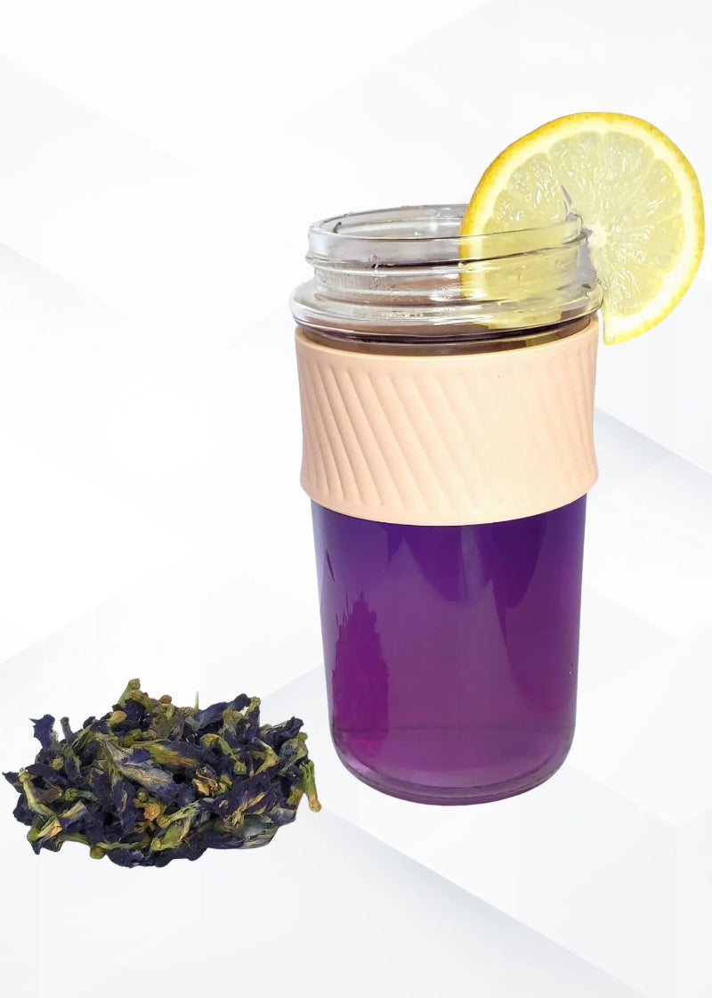 Purple liquid in a glass container with a lemon slice and dried tea leaves on a white background